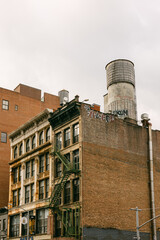 Red brick building with fire escape and water tower in urban setting during cloudy day