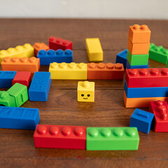 Naklejka premium Colorful plastic building blocks scattered and stacked on a wooden table, featuring a yellow block with a happy smiley face.
