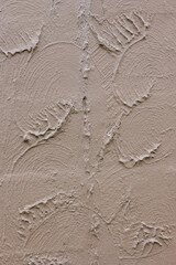 Textured wall with swirling patterns and leaf-like designs created from plaster work in a sunny room