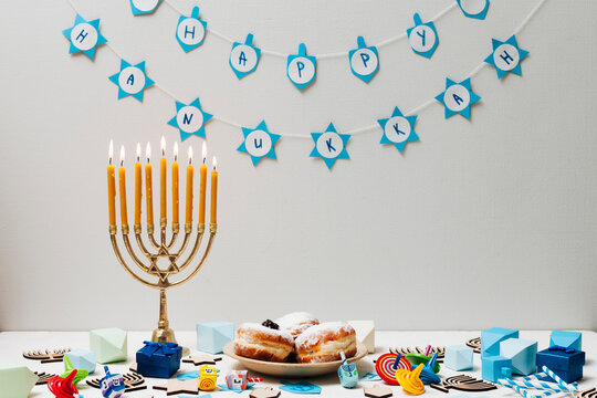 Festive hanukkah celebration with lit menorah delicious sufganiyot pastries and decorative banner against a plain wall
