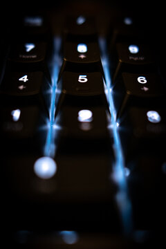 Extreme close-up of a backlit keyboard's numeric pad. The dark, high-contrast image highlights the glowing numbers and blue light, creating a modern, techy, and futuristic vibe.