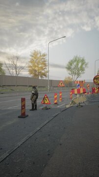 A dedicated road worker stands near construction barriers on a city street, ensuring safety while directing traffic amid colorful fall foliage in the background.