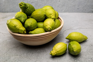 Fresh green lemons in a wicker bowl on concrete
