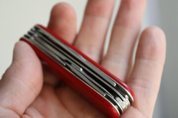 A person's hand holding a red Swiss Army knife, suitable for illustrations on adventure, travel or outdoor activities