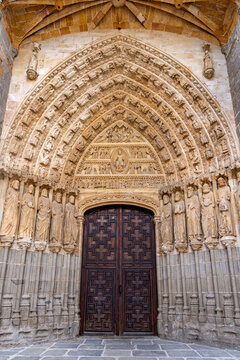 A striking close-up of &Aacute;vila Cathedral&rsquo;s Gothic side portal, with a tall pointed arch of carved archivolts above massive patterned wooden double doors and rich sculptural detail