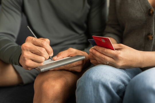 Couple reviewing credit cards and writing down expenses for budgeting at home - Powered by Adobe
