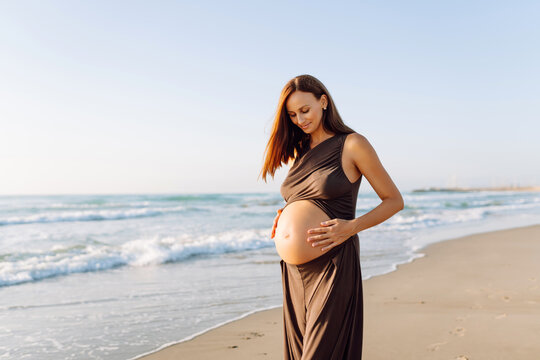 A pregnant woman stretches on a yoga mat by the sea at sunset. A beautiful woman expecting a child meditates or stretches outdoors, enjoying the seascape. The concept is relaxation and rest.