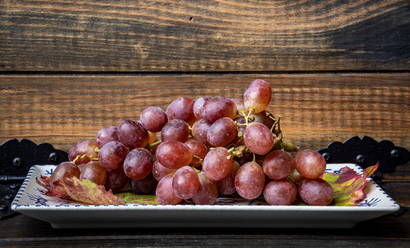 Uvas rojas frescas dispuestas en una superficie de madera, creando un castraste visual con gotas de agua en las hojas de la parra a&ntilde;aden un aspecto fresco y apetitoso