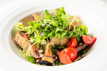 gourmet salad with mixed greens, tomatoes, fried items (likely eggplant or tofu), meat slices, and seeds in a white bowl, perfect for food, healthy eating, and restaurant concepts.