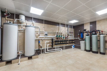 A utility room is filled with a modern plumbing system. Two large water heaters are connected to various pipes. Well-organized valves and tanks are visible along the walls