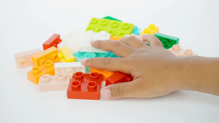 Asian boy's hand on a pile of small plastic blocks or plastic blocks of various shapes, sizes, and colors that can be connected and assembled into various shapes, isolated on white background © PinkyEn