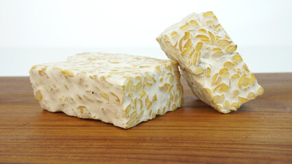 Tempeh or soybean cake, a source of vegetable protein made from boiled soybeans and given yeast through a fermentation process to form a solid, on a wooden cutting board