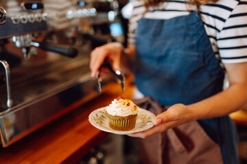 A vibrant berry cake with fresh cupcakes stands in the cozy bakery's window. Fragrant desserts in the coffee shop. Food concept, small business.