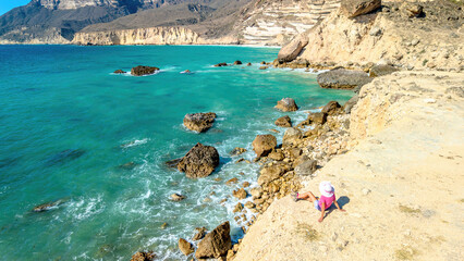 aerial view of a tourist woman exploring shore of Al Fizayah in Salalah, Oman. A traveler marvels at dazzling contrast of white sand and turquoise sea, surrounded by majestic Salalah's coastal city.