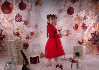 Kleines lachendes M&auml;dchen mit rotem Kleid freut sich &uuml;ber die Weihnachtsgeschenke. 