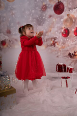 Kleines lachendes M&auml;dchen mit rotem Kleid freut sich &uuml;ber die Weihnachtsgeschenke. 