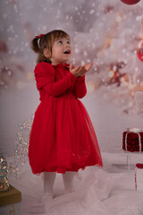 Kleines lachendes M&auml;dchen mit rotem Kleid freut sich &uuml;ber die Weihnachtsgeschenke. 