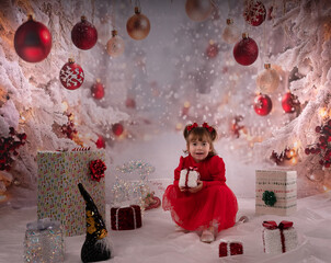 Kleines lachendes Mädchen mit rotem Kleid freut sich über die Weihnachtsgeschenke. 
