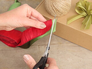 Woman wrapping gifts. Preparing for Christmas. Woman cutting a red and a green satin ribbon with a scissor.	