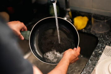 Man washing frying pan under running water