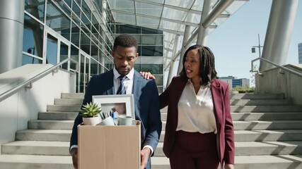 Sad businessman leaving office with box of belongings supported by colleague offering comfort during a career change, capturing empathy and corporate support