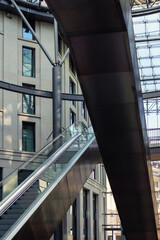 Fototapeta premium Empty escalator rises inside bright modern commercial atrium with clean steel and glass structure. Symmetric lines, soft reflections airy architecture create spacious contemporary urban atmosphere