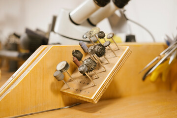 Rotary tool burrs polishing jewelry bench microscope workshop with assortment of abrasive heads on wooden block for metalwork and gemstone finishing in studio workspace