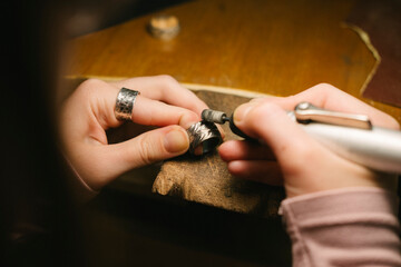 Jewelry ring hands polishing workshop tool craftsman metal working on a wooden bench using a rotary tool to refine a silver ring closeup showing skill manual craft and delicate finishing details
