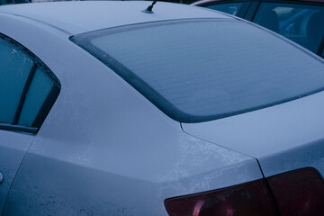 Frost car window with ice and snow on rear glass of parked sedan, cold morning with frozen windshield and icy texture on roof and trunk, winter maintenance and deicing concept