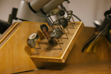 Rotary burrs polishing tools on wooden block in jewelry workshop, metal brushes and grinding bits for precision shaping and finishing, bench equipment for repair and craft work