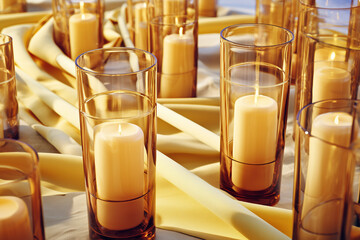 Soft glowing candles in amber glass holders on yellow fabric creating warm festive atmosphere for holiday decor concept of interior design and event styling