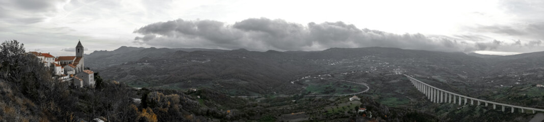 Panoramic view showing Gairo Vecchio village, Sardinia landscape, and long viaduct on cloudy day