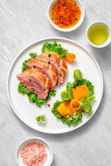 Delicious roasted duck breast fillet with golden crispy skin, with pepper and rosemary, top view on ceramic white plate, rustic concrete rustic background

