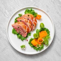 Delicious roasted duck breast fillet with golden crispy skin, with pepper and rosemary, top view on ceramic white plate, rustic concrete rustic background