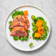 Delicious roasted duck breast fillet with golden crispy skin, with pepper and rosemary, top view on ceramic white plate, rustic concrete rustic background