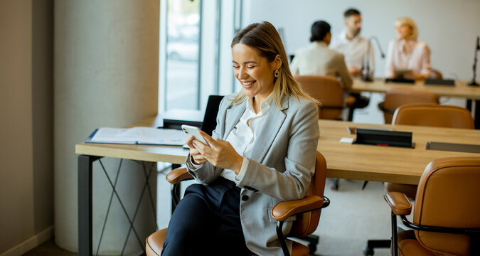Smiling woman in office checking phone during business meeting hours