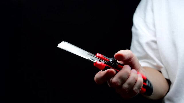 An office worker holds a red retractable utility knife.
The person is holding the sharp blade of the knife.
Utility knife, steel, cutter, tool, instrument