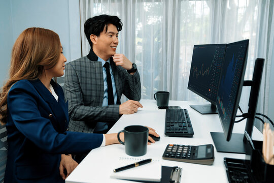 Smiling business Asian coworkers discussing dynamic stock market graph report on computer comparing value exchange data online program at modern office. Analyzing rate investment company. Infobahn.