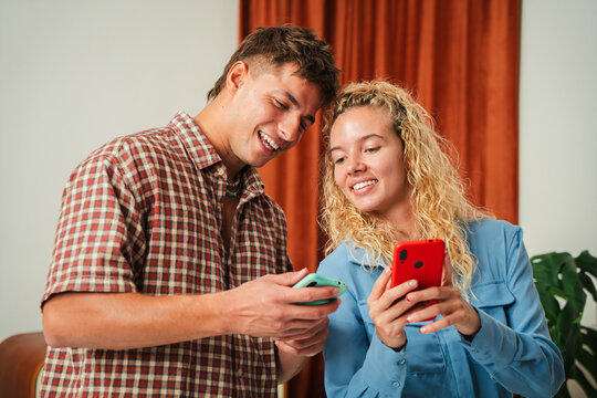 Joyful young couple engages with their smartphones, sharing delightful moments and laughter together as they explore various apps and content, radiating happiness and connection in their interaction.