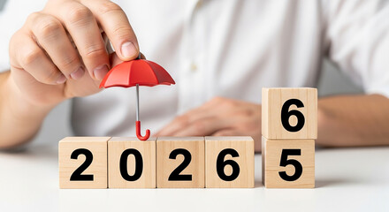 A hand holding a red umbrella over wooden blocks spelling out the year twenty twenty six sixty five 