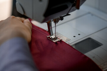 Close-up of a seamstress's hand working on a machine with burgundy fabric.