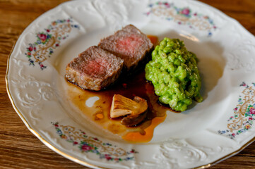 Juicy medium-rare steak with green pea puree and mushrooms on a vintage plate.
