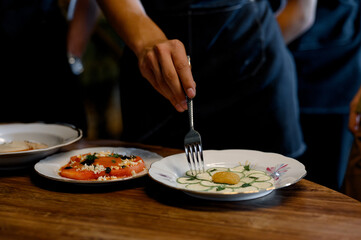A waiter's hand with a fork decorates a plate with fresh vegetables.