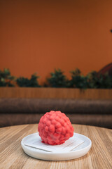 Close-up image of a raspberry shaped red dessert placed on a white ceramic plate on a wooden table.