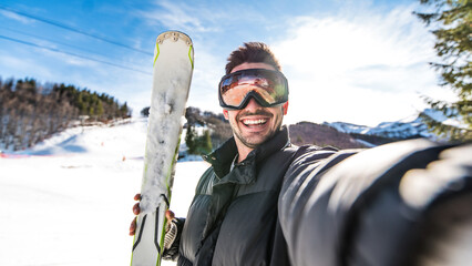 Fototapeta premium Happy skier taking selfie pic with smart cell phone device outside - Young man having fun on weekend activity in ski resort vacation - Winter sport concept