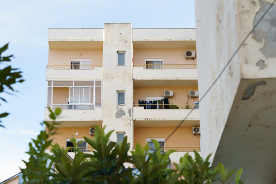 A simple city building with small balconies and an aging exterior AC unit. Ideal for rental listings, affordable housing searches, and foreign real estate exploration.