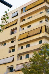 Obraz premium A compact yellow residence with functional terraces and air-conditioning units. Great for holiday rentals, furnished city apartments, property searches, and long-term investment in coastal towns.