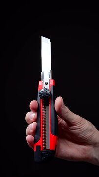 An office worker holds a red retractable utility knife.
The person is holding the sharp blade of the knife.
Utility knife, steel, cutter, tool, instrument