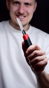 An office worker holds a red retractable utility knife.
The person is holding the sharp blade of the knife.
Utility knife, steel, cutter, tool, instrument