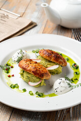 Two golden-brown biscuits filled with creamy green spread sit elegantly on a white plate. Fresh radish slices, herbs, and vibrant sauce create an inviting dining experience